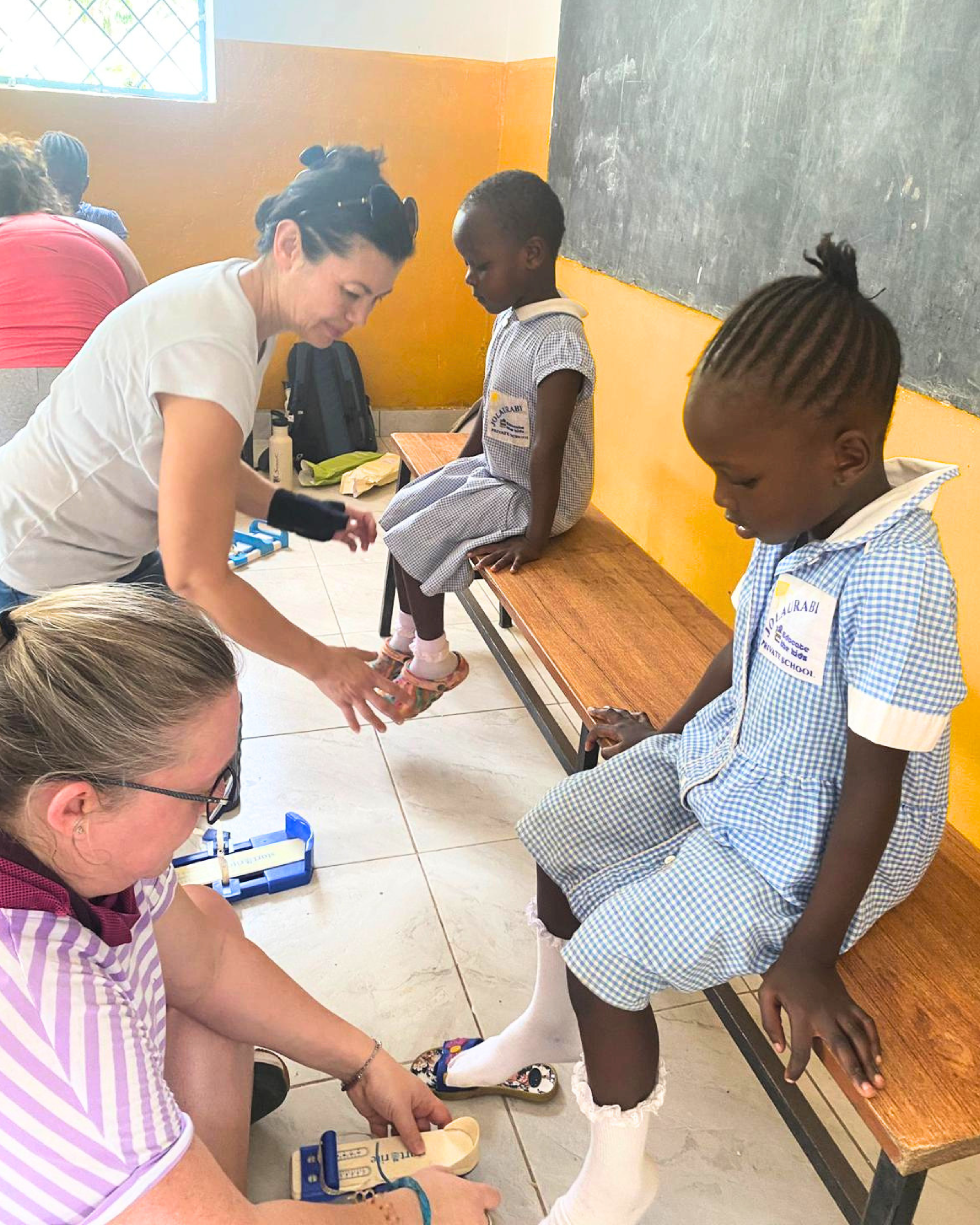 Two volunteers fitting shoes on schoolchildren in uniform during a charitable outreach program in Africa.