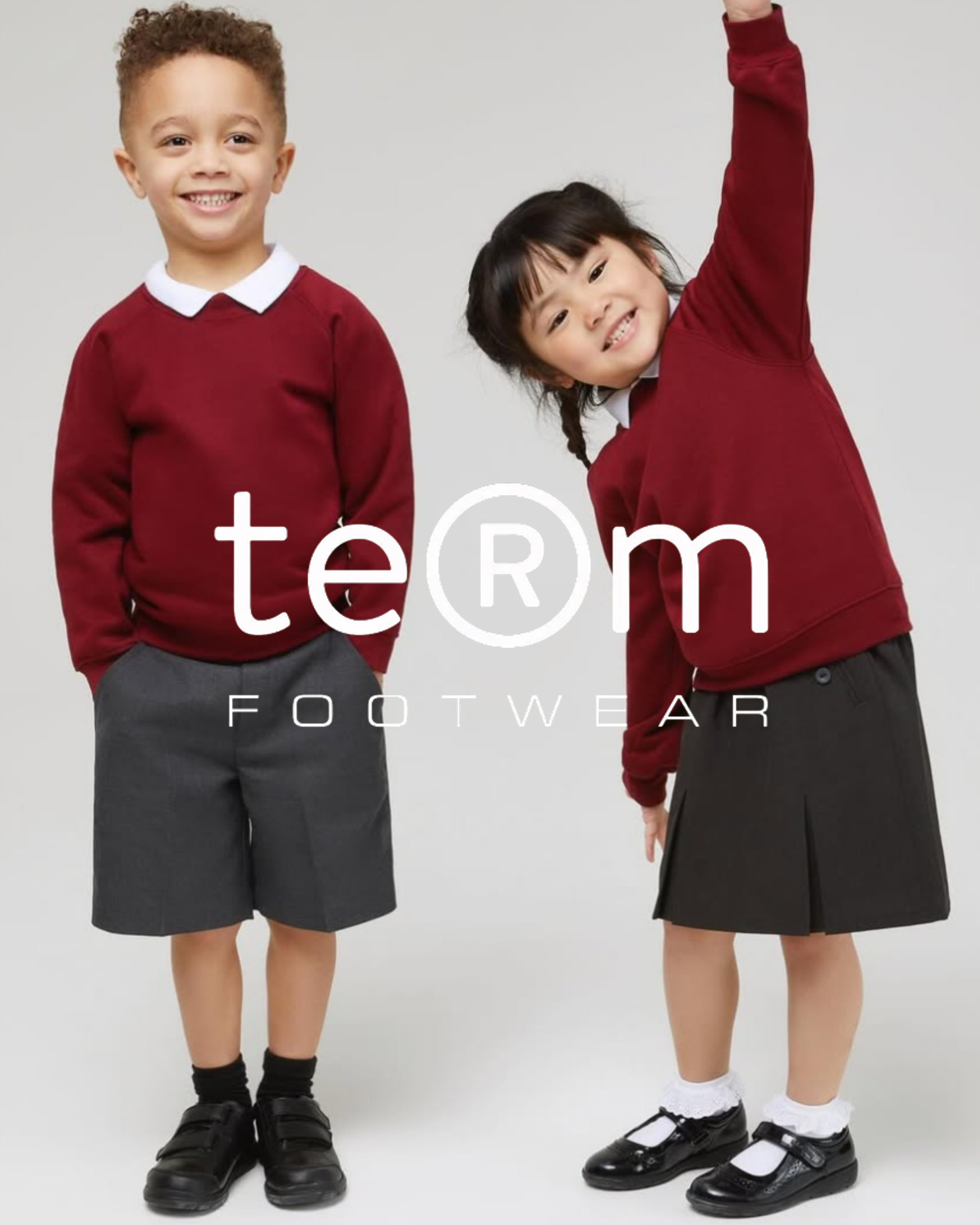 Two young children in school uniforms wearing black school shoes from Term Footwear, smiling against grey background.