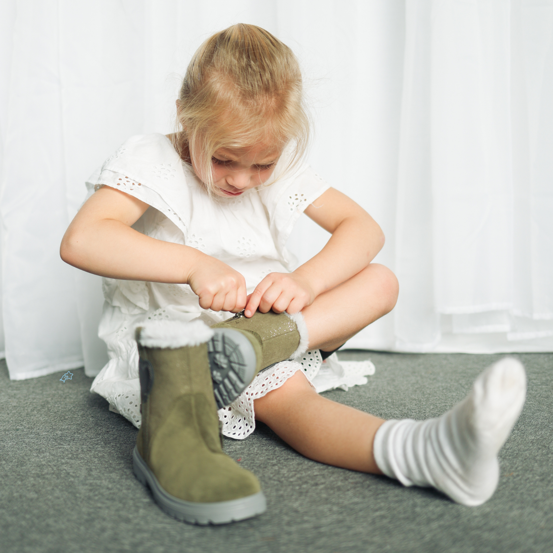 Young girl sitting on floor putting on olive green fur-lined winter boots with white socks