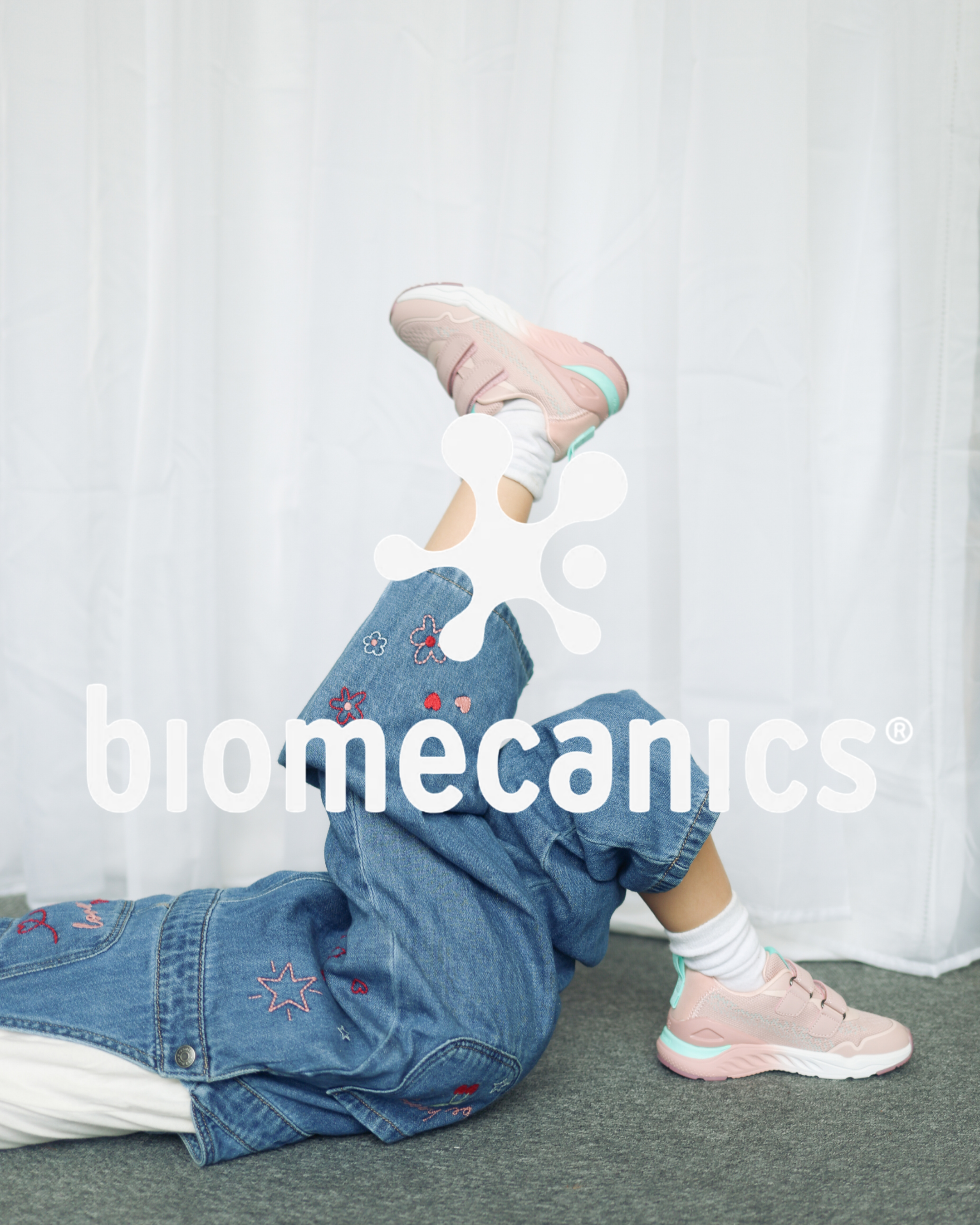 Child lying down wearing pink and mint Biomecanics trainers with embroidered denim jeans