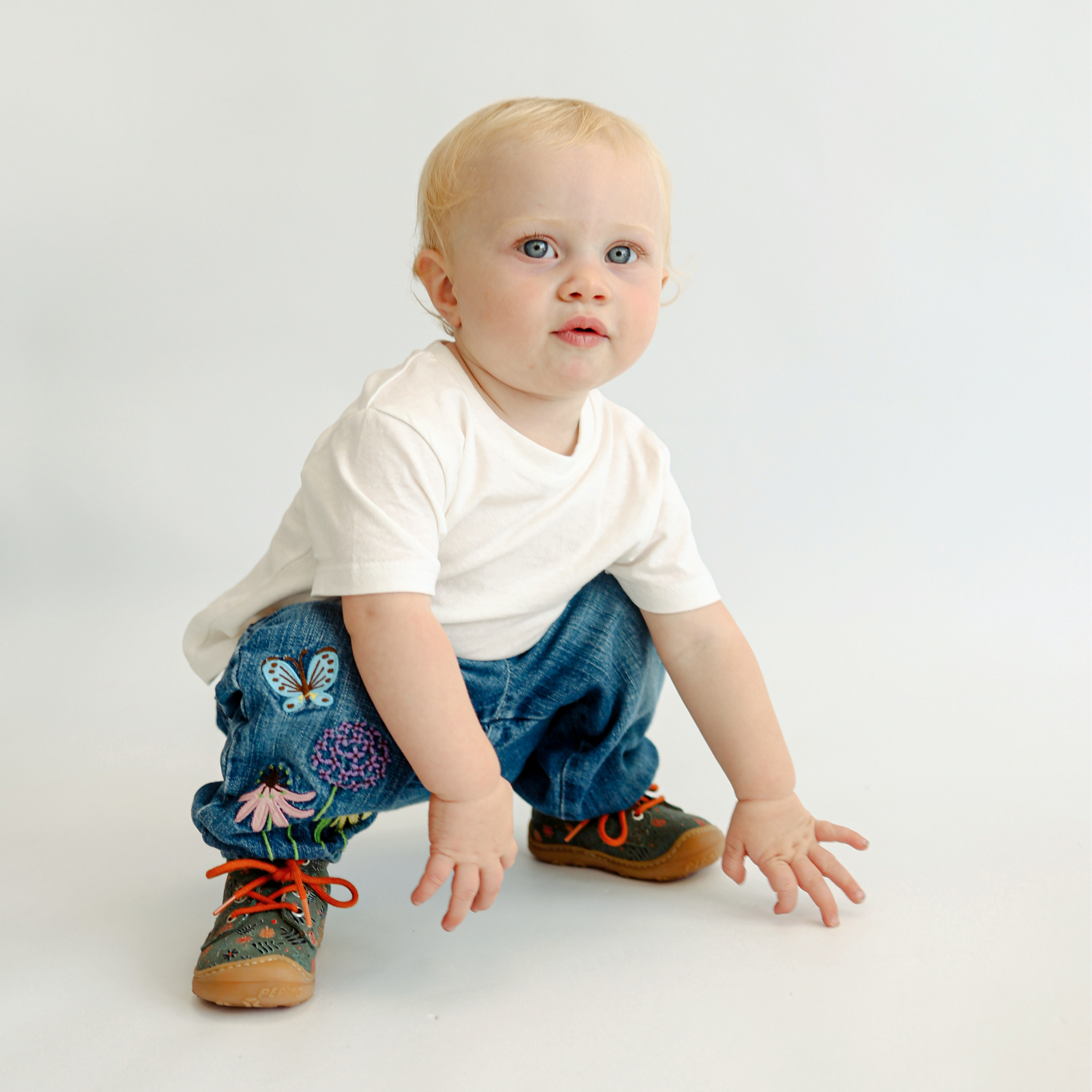 Toddler wearing ShuZu dark green boots with orange laces, paired with floral jeans and white t-shirt