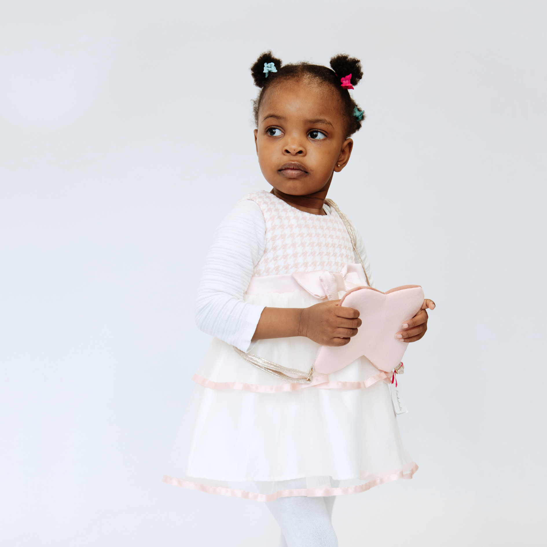 Toddler girl in pink houndstooth dress holding a star purse, wearing white tights, with colorful hair clips