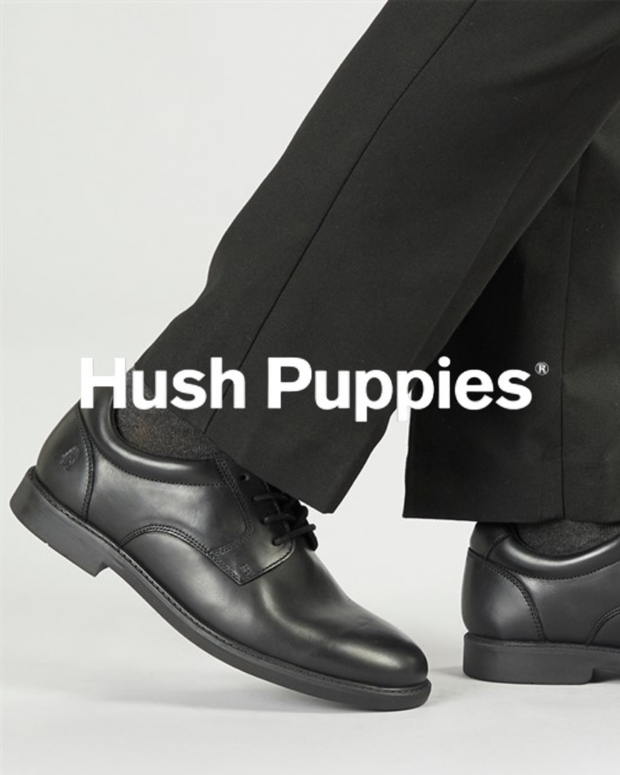 Hush Puppies black leather lace-up school shoes worn with black trousers, shown from the ankle down.