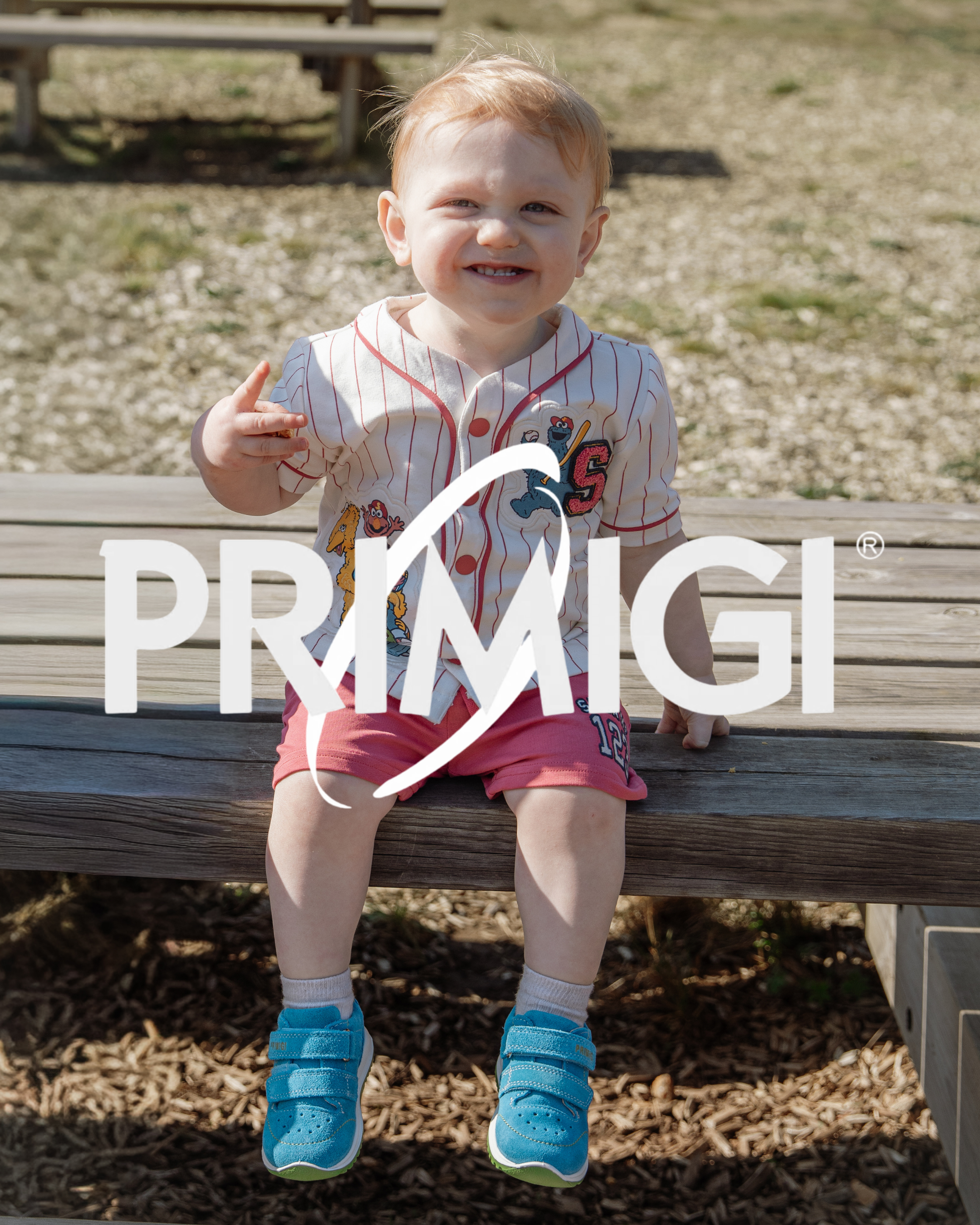 Smiling toddler sitting on a bench wearing bright blue Primigi velcro trainers with a Sesame Street outfit.