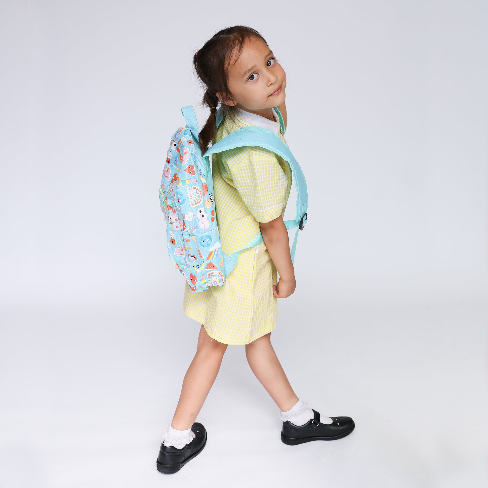 Girl in yellow gingham dress wearing a blue backpack and black Mary Jane school shoes with white ankle socks.